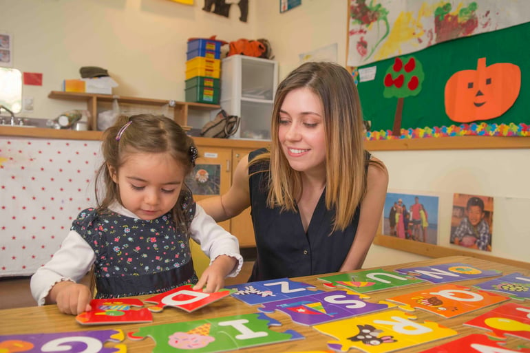 teacher helps girl with alphabet puzzle